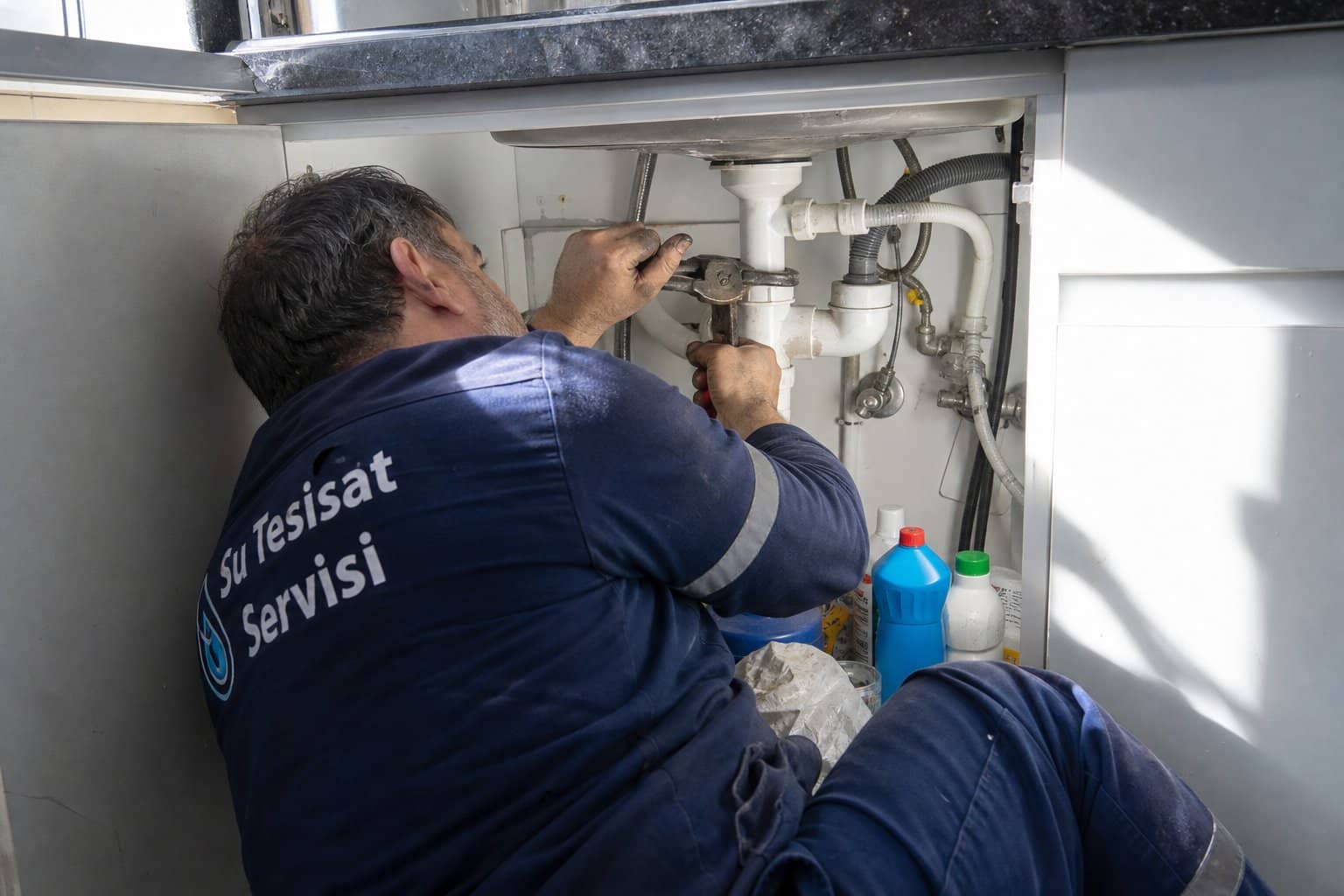 Lavabo altında boru anahtariyla boru tamir eden tesisatçı